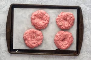 four hamburger patties on a baking sheet.