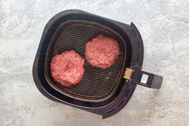 hamburger patties in an air fryer basket.