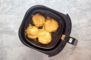 air fried burger patties with cheese in an air fryer basket.