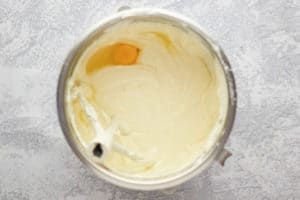 adding an egg to cheesecake filling mixture in a mixing bowl.