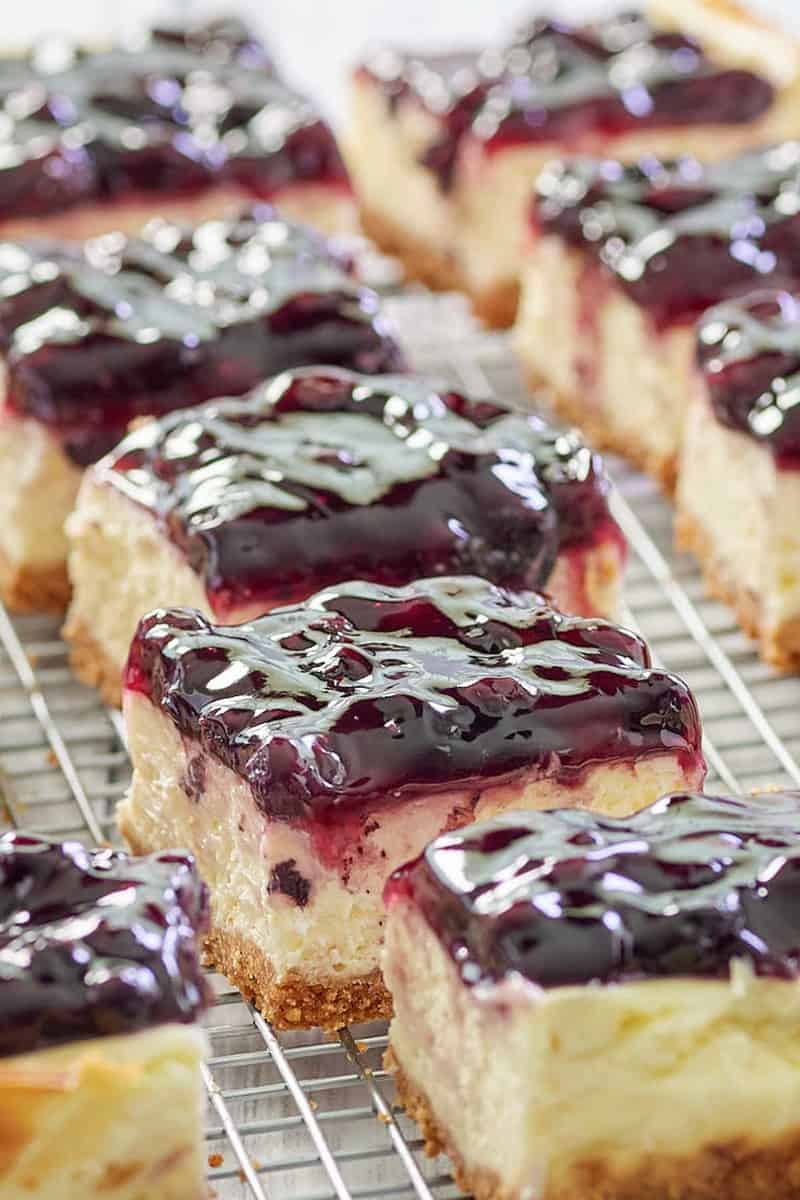 blueberry cheesecake bars in rows on a wire rack.