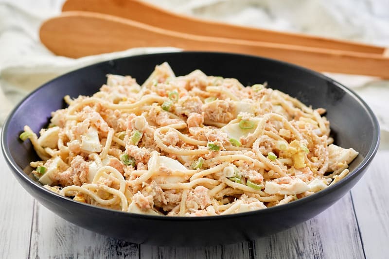 shrimp pasta salad in a trencher and wood salad tongs.