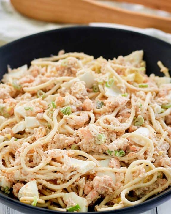 cold shrimp pasta salad in a bowl and wood salad tongs.
