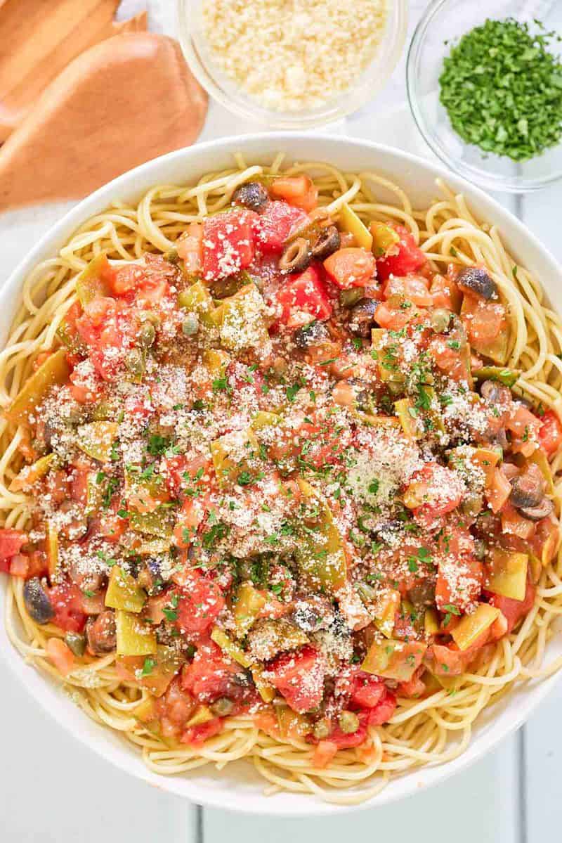 overhead view of spaghetti alla puttanesca, parmesan cheese, and chopped parsley.