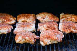 dry rubbed chicken thighs on a smoker rack.