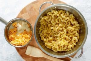 cooked macaroni in a strainer and cheese sauce ingredients in a saucepan.
