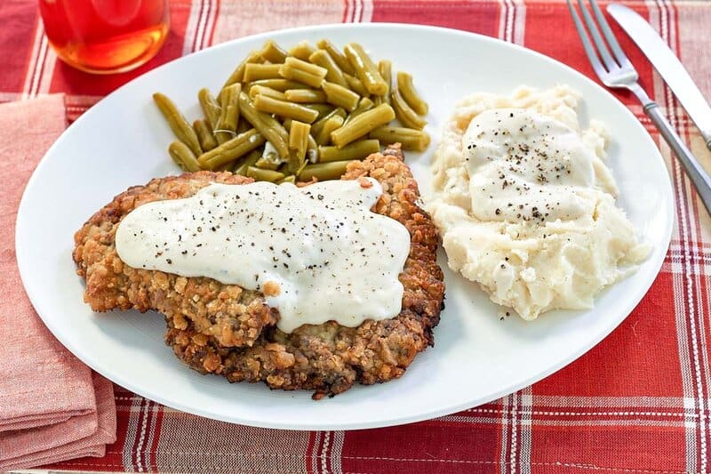 copycat Cracker Barrel country fried steak, sides, and gravy on a plate.