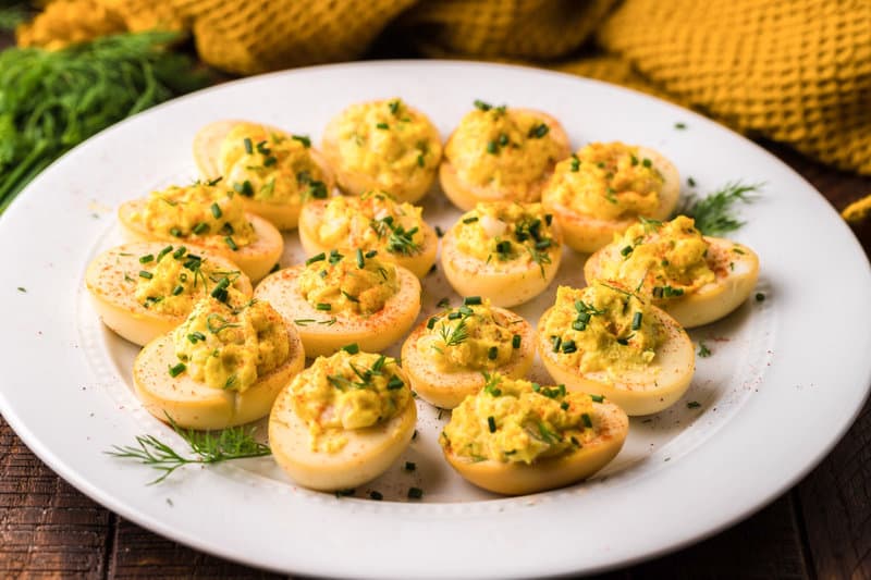 smoked deviled eggs topped with herbs on a white platter.
