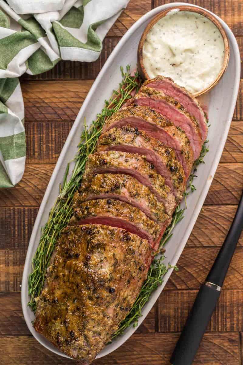 overhead view of smoked eye of round roast and horseradish sauce on a platter.