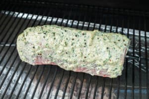 eye of round roast coated with horseradish sauce on a smoker grate.