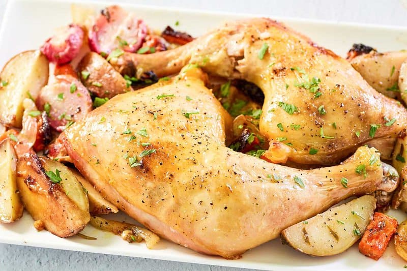 two baked chicken leg quarters and vegetables on a platter.