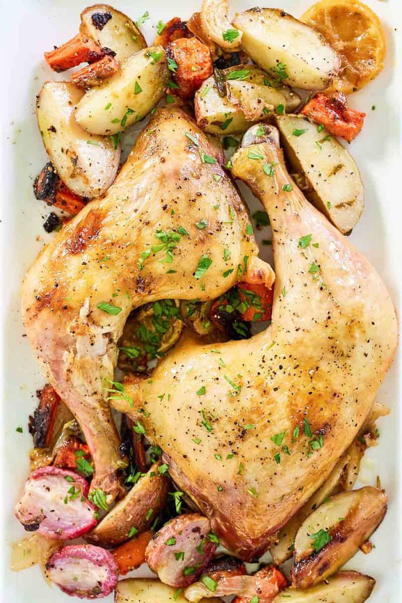 overhead view of baked chicken leg quarters and vegetables on a white platter.