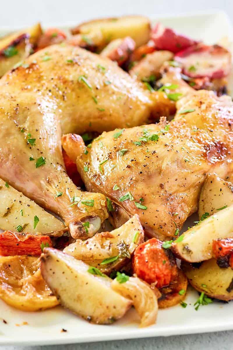 two baked chicken leg quarters with vegetables on a platter.