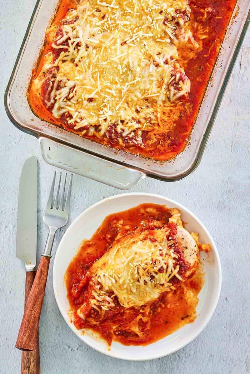 overhead view of baked chicken parmesan on a plate and in a baking dish.