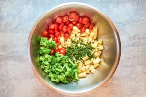 broccoli pasta salad ingredients in a large stainless steel mixing bowl.