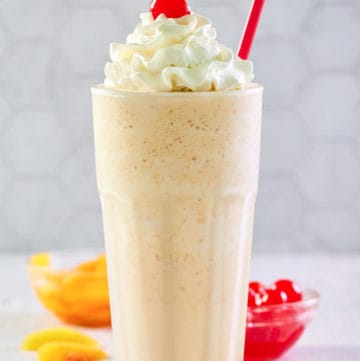 copycat Chick Fil A peach milkshake with whipped cream and a cherry.