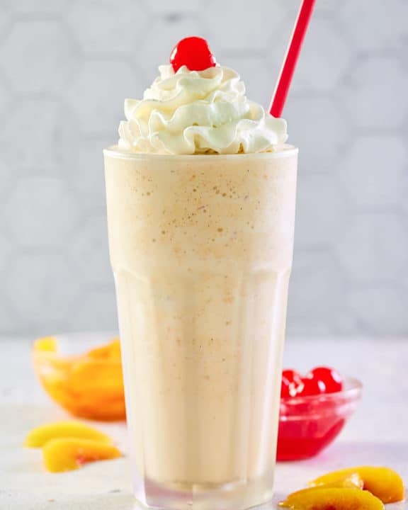 copycat Chick Fil A peach milkshake with whipped cream and a cherry.