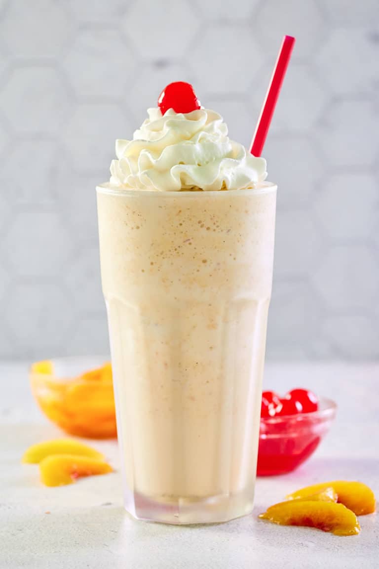 copycat Chick Fil A peach milkshake with whipped cream and a cherry.