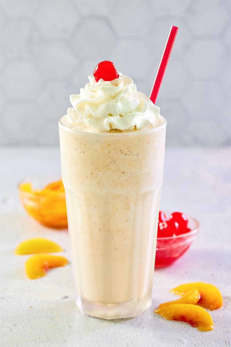 copycat Chick Fil A peach milkshake topped with whipped cream and a cherry.