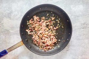 cooked bacon pieces and onions in a skillet.