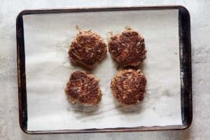 four cooked hamburger steaks on a baking sheet.