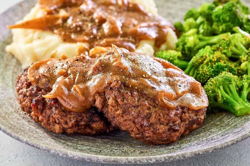 two copycat Cracker Barrel hamburger steaks and gravy on a plate.