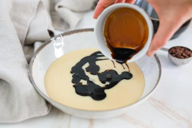 pouring butter pecan flavoring into a bowl of sweetened condensed milk.