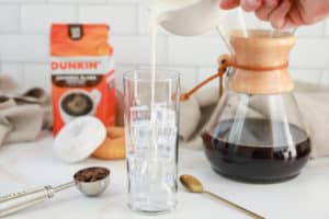 pouring half and half over ice in a glass.