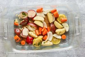 chopped vegetables, lemon slices, and herbs in a baking dish.