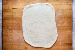 pizza dough rolled out on a wood board.
