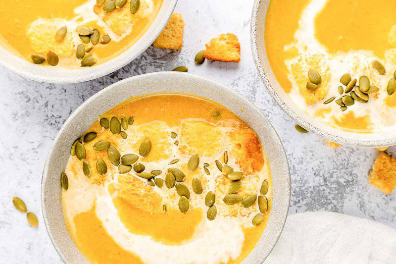 three bowls of pumpkin bisque topped with croutons and pepitas.