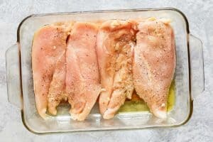 four seasoned chicken breasts in a glass baking dish.