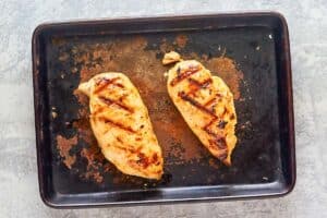 two grilled chicken breasts on a baking sheet.