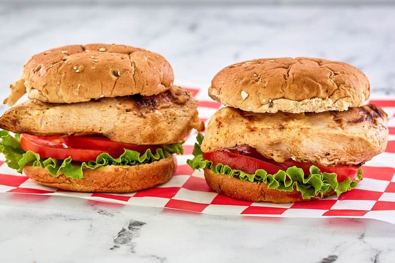 two copycat Chick Fil A grilled chicken sandwiches with lettuce and tomato.
