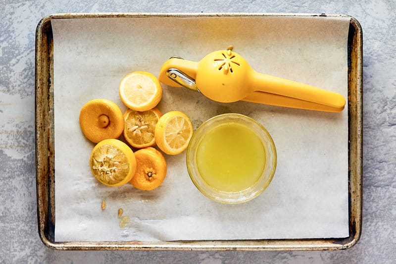 lemon squeezer, squeezed lemons, and bowl of lemon juice on a tray.