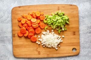chopped carrots, celery, and onions on a cutting board.
