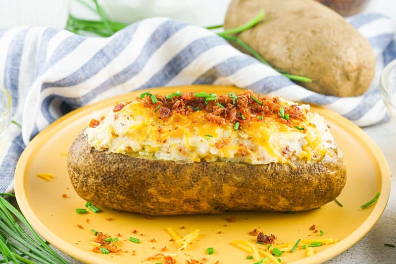loaded twice baked potato on a plate and a potato behind it.