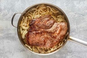 brown beef roast and onions in a pan.