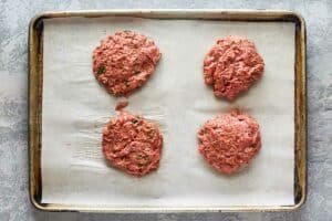 four uncooked turkey burger patties on a tray.