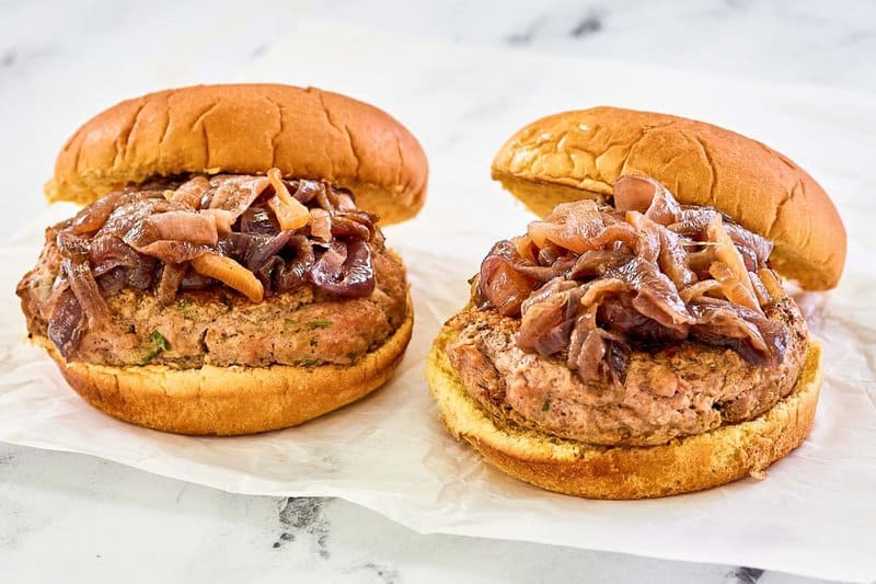 two turkey burgers with caramelized red onions on parchment paper.