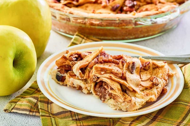 slice of apple pie cheesecake and two apples.