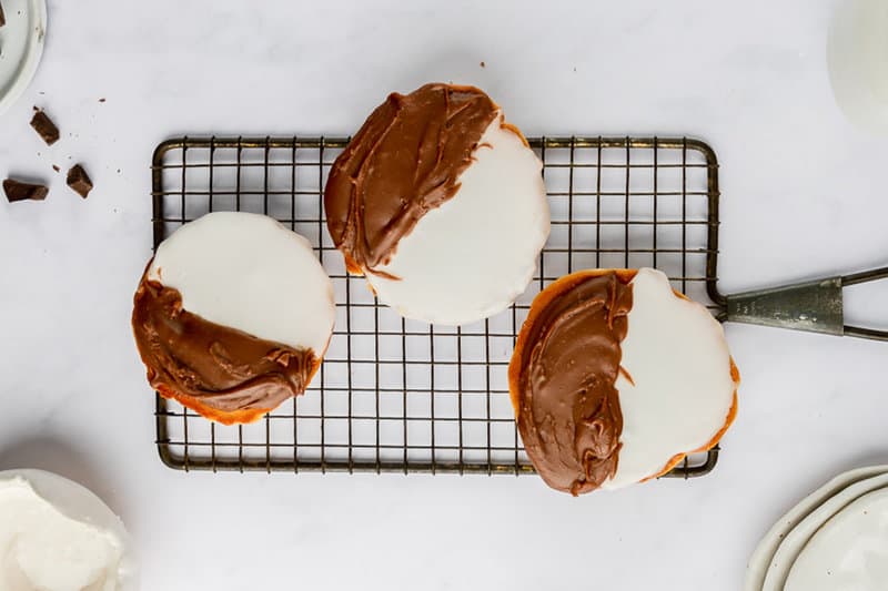 three black and white cookies on a wire rack.