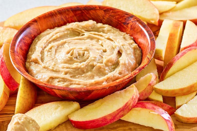 caramel apple dip in a bowl and sliced apples around it.