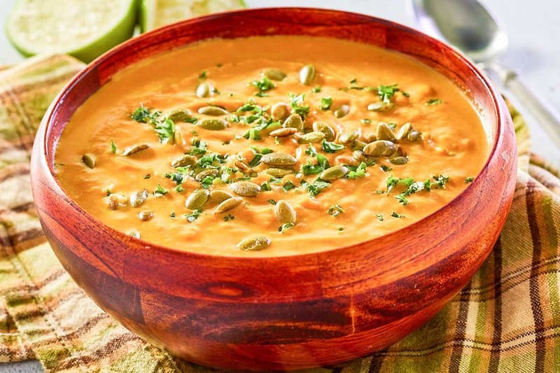 bowl of pumpkin curry soup topped with pepitas and chopped parsley.