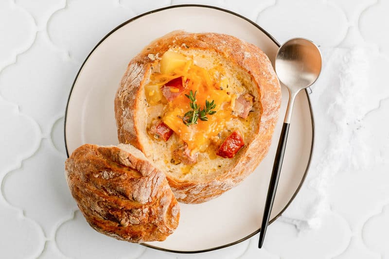 overhead view of sausage stew in a bread bowl on a plate and a spoon.