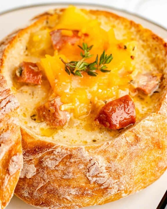 sausage stew topped with cheddar cheese in a bread bowl.