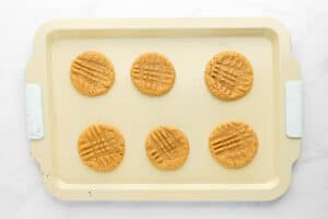 six baked peanut butter cookies on a baking sheet.