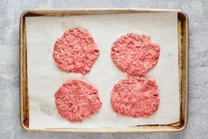 raw hamburger patties on a tray.