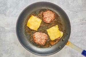cooking hamburger patties with cheese in a skillet.