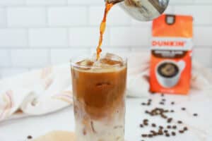 pouring espresso into a glass with milk, ice, and caramel.